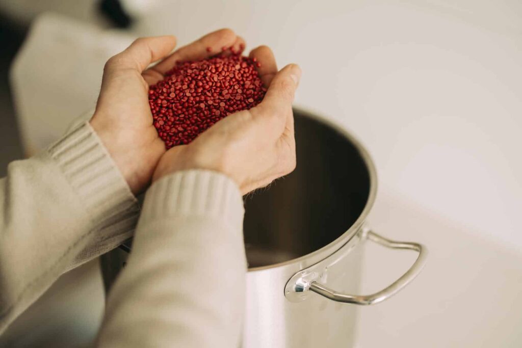 Mains tenant des pastilles colorées au-dessus de la cuve de fusion de cire